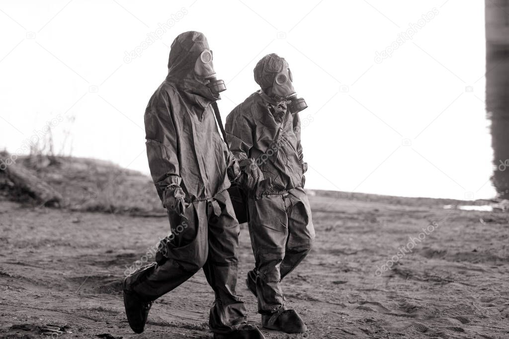 Two persons walks in NBC protective suits and gas masks. Concept of a preventive measures and protection for coronavirus COVID 19 pandemic and other global dangers.