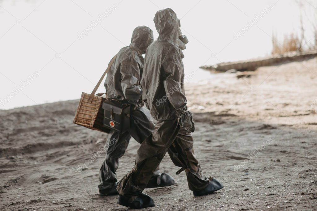 Two persons walks in NBC protective suits and gas masks. Concept of a preventive measures and protection for coronavirus COVID 19 pandemic and other global dangers.