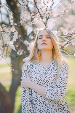 Genç sarışın bir kadın bahar çiçekli kayısı ağaçlarının arasında duruyor..