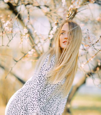 Genç sarışın bir kadın bahar çiçekli kayısı ağaçlarının arasında duruyor..