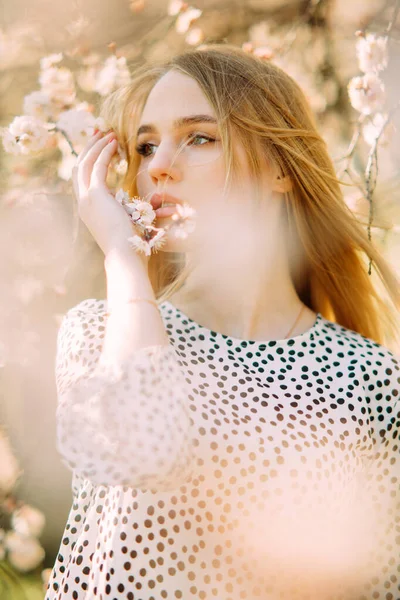 Bahar bahçesinde çiçek açan kayısı ağaçlarının arasında genç sarışın kadın portresi..