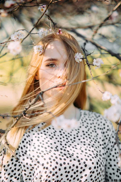 Bahar bahçesinde çiçek açan kayısı ağaçlarının arasında genç sarışın kadın portresi..