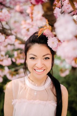 Beyaz elbiseli genç kadın, sakura ağaçlarıyla parkta rahatlıyor ve eğleniyor. Portre.