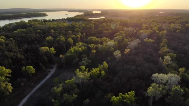 Relevé aérien par drone au-dessus de la forêt et sentier le long de la rivière au coucher du soleil. Au loin peut être vu bateau sur la rivière et le village .