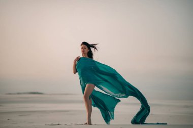 Çölde poz veren mavi dokuya sarılmış bir kadın..