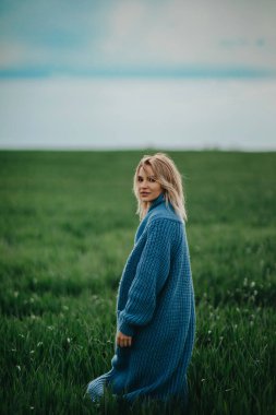 Mavi ceketli genç bir kadın buğday tarlasında yürüyor..