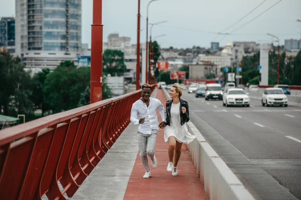 인종간의 남녀가 뛰어다니며 도시와 도로의 배경에서 유쾌하게 웃는다 인종간 관계와 — 스톡 사진