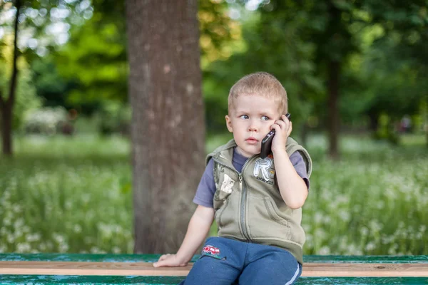 Jongetje praten aan de telefoon buitenshuis zittend — Stockfoto