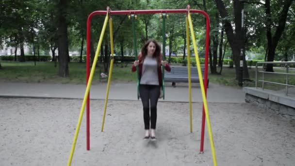 Jonge mooie vrouw is plezier op een schommel onder een boom in de natuur. — Stockvideo