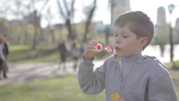 El chico está jugando con burbujas de jabón. Un niño pequeño sopla burbujas — Vídeos de Stock