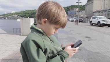 Genç çocuk smartphone şehir içinde oynamaya. Cep telefonu olan çocuk. Küçük çocuk sokakta smartphone ile oynamak