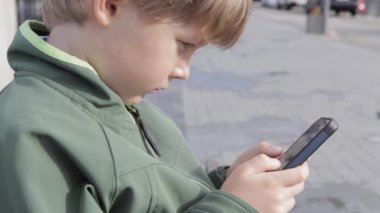 Genç çocuk smartphone şehir içinde oynamaya. Cep telefonu olan çocuk. Küçük çocuk sokakta smartphone ile oynamak