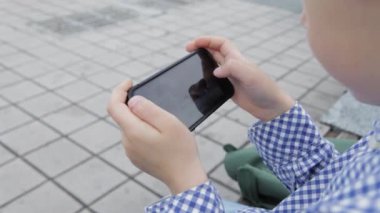 Genç çocuk smartphone şehir içinde oynamaya. Cep telefonu olan çocuk. Küçük çocuk sokakta smartphone ile oynamak