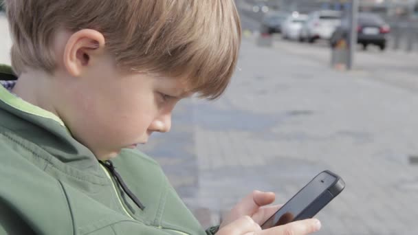 Ragazzo che gioca sullo smartphone in città. Ragazzo con il cellulare. Ragazzino per strada che gioca con lo smartphone — Video Stock