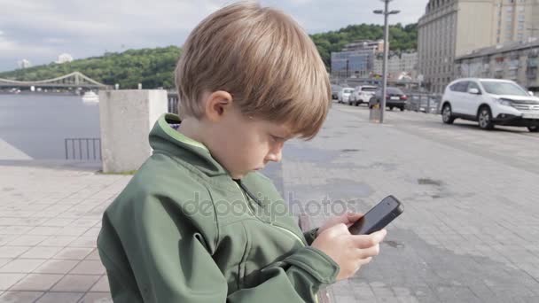 Ragazzo che gioca sullo smartphone in città. Ragazzo con il cellulare. Ragazzino per strada che gioca con lo smartphone — Video Stock