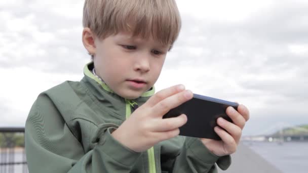 Niño jugando en el teléfono inteligente en la ciudad. Niño con teléfono móvil. Niño en la calle jugando con el teléfono inteligente — Vídeo de stock