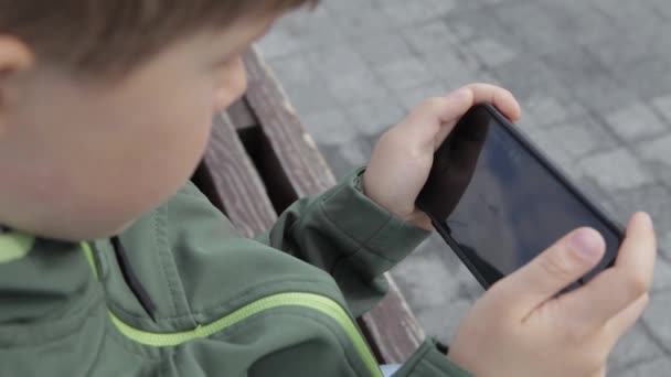 Fiatal fiú játék-ra smartphone a városban. Fiú-val mozgatható telefon. Az utcán játszó smartphone kisfiú — Stock videók