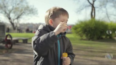Küçük sarışın bir çocuk sokakta oynuyor. Balonlar uçurdu. Genç çocuk kabarcıklar, yavaş üfleme.