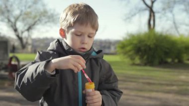 Küçük sarışın bir çocuk sokakta oynuyor. Balonlar uçurdu. Genç çocuk kabarcıklar, yavaş üfleme.