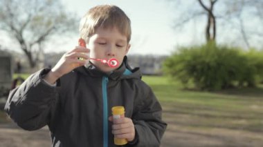 Küçük sarışın bir çocuk sokakta oynuyor. Balonlar uçurdu. Genç çocuk kabarcıklar, yavaş üfleme.