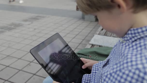 O rapaz está a brincar no tablet. Um rapazinho com um tablet electrónico nas mãos . — Vídeo de Stock