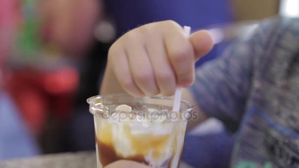 一个小男孩在一家咖啡馆吃冰激淋。在咖啡馆里的金发男孩用勺子吃冰激淋. — 图库视频影像