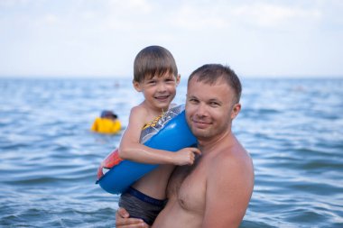 Küçük bir çocuk ile babası denizde yüzüyor.