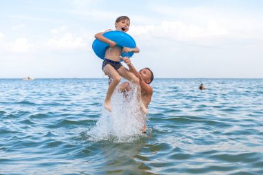 Baba ve oğlu denizde banyo, eğlenceli oyun. Baba oğlunu suya atar..