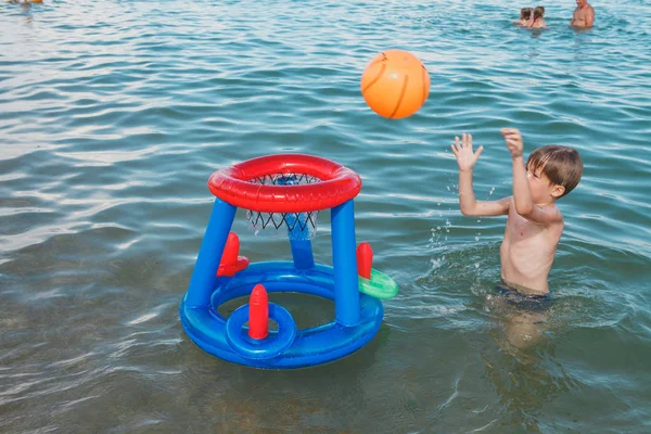 Sahilde su ile bir şişme top oynayan bir çocuk. Küçük çocuk su basketbol oynarken.