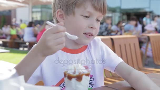 Il mange de la glace. Blonde garçon manger de la crème glacée regardant la caméra . — Video