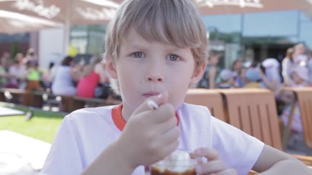 Blond boy äta glass tittar på kameran. Pojken äter en glass sked. — Stockvideo