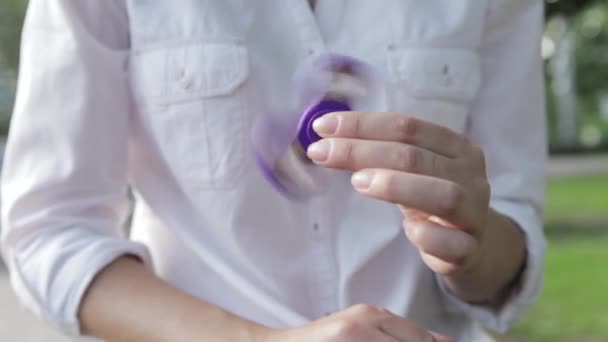 En tjej leker med en snurrande leksak, snurrande i handen. Den flicka twirks spinner i fria — Stockvideo