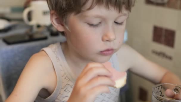 De jongen eet een sandwich, en drankjes. De jongen is ontbijten. — Stockvideo