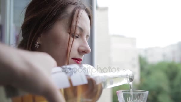 La chica se vierte una copa de vino blanco. Una joven bebe vino blanco junto a la ventana. . — Vídeo de stock