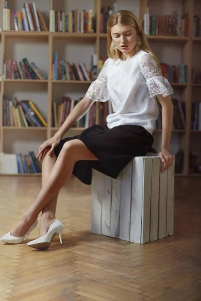 Estudante de glamour bonito na biblioteca. Ela está sentada na lama. — Fotografia de Stock