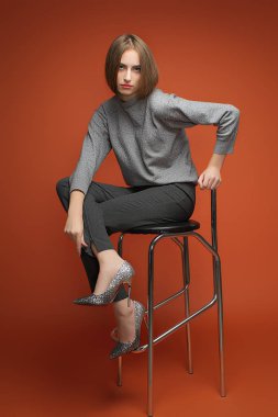 Girl sits crossing fits. Style in grey. Office look. Female beauty concept. Portrait of fashionable young  in classic clothes clipart