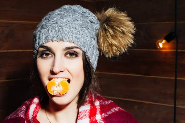 Jovem bela mulher de cabelos escuros sorrindo em roupas de inverno e boné com tangerinas no fundo de madeira . — Fotografia de Stock