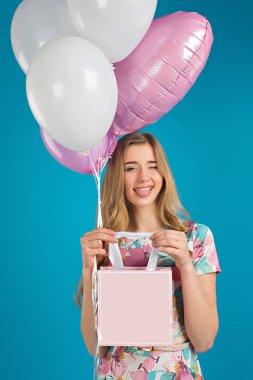 Baloons ve mavi arka plan üzerinde elinde küçük prersents çanta ile tatlı güzel kız.