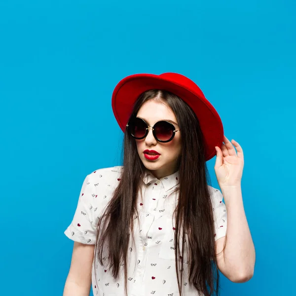 Mode jolie jeune femme soufflant rouge à lèvres portant un chapeau noir lunettes de soleil et chapeau rouge — Photo