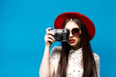 Moda güzel genç gülümseyen kadın retro kamera kırmızı şapka, mavi arka plan üzerinde tutar.