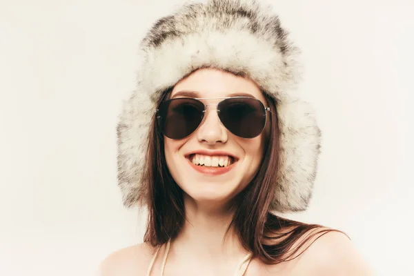 Красивая и счастливая молодая женщина изолированы на белом и носить меховую шапку и солнцезащитные очки — стоковое фото