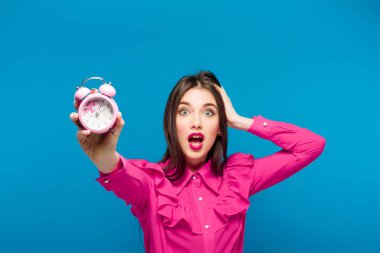 Mavi bir arka plan üzerinde bir saat tutan genç kadın