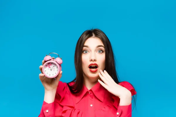 Mujer joven sosteniendo un reloj sobre un fondo azul —  Fotos de Stock
