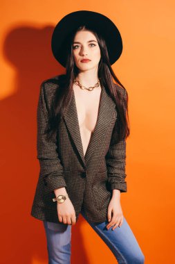 kahverengi ceketli Studio'da güzel bir kız güler. Turuncu arka plan. Şapka