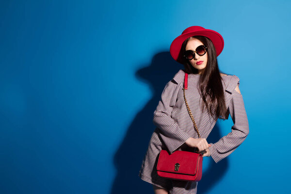 Lovely model in fashionable red Hat and a red Clutch on blue background