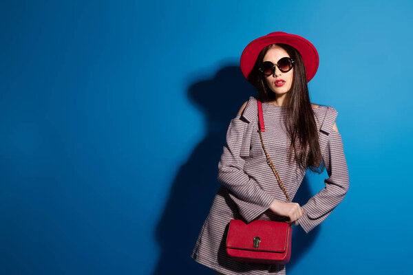 Lovely model in fashionable red Hat and a red Clutch on blue background