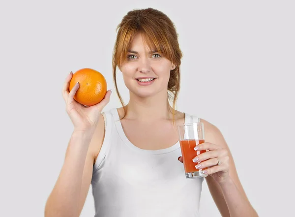 Mujer deportiva sobre fondo gris sosteniendo vaso de zumo de pomelo — Foto de Stock