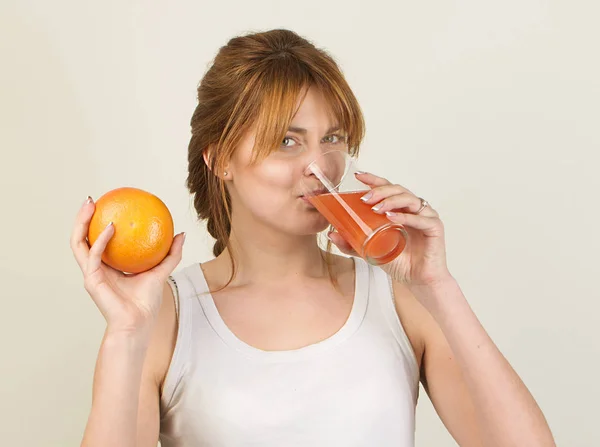 Mujer deportiva sobre fondo gris sosteniendo vaso de zumo de pomelo — Foto de Stock