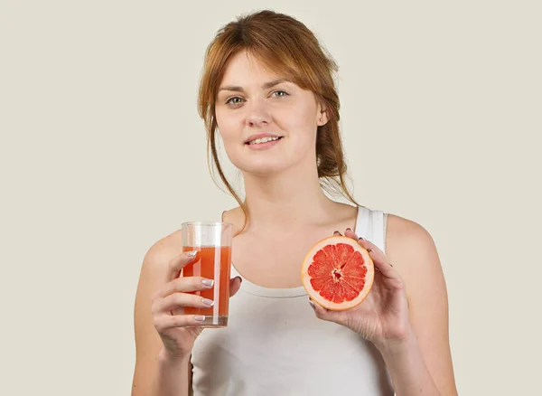 Mujer deportiva sobre fondo gris sosteniendo vaso de zumo de pomelo — Foto de Stock