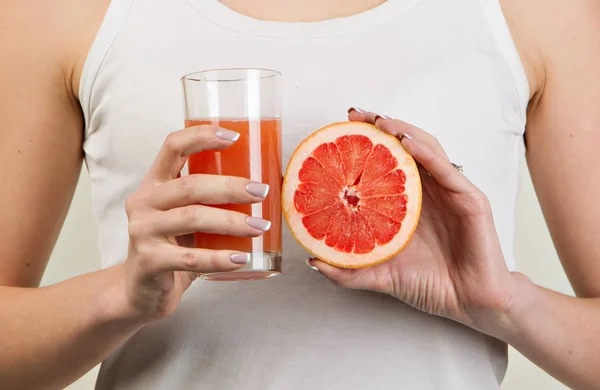 Mujer deportiva sobre fondo gris sosteniendo vaso de zumo de pomelo — Foto de Stock